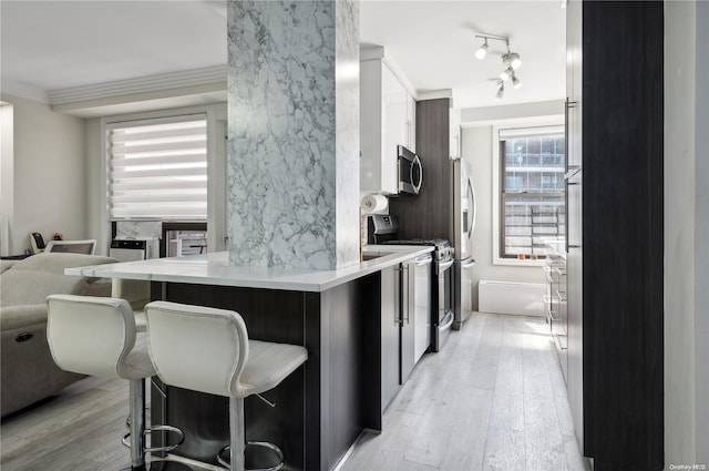 kitchen with kitchen peninsula, appliances with stainless steel finishes, light hardwood / wood-style floors, and a breakfast bar area