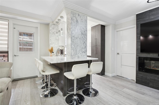 interior space with kitchen peninsula, crown molding, a fireplace, light hardwood / wood-style floors, and a breakfast bar area