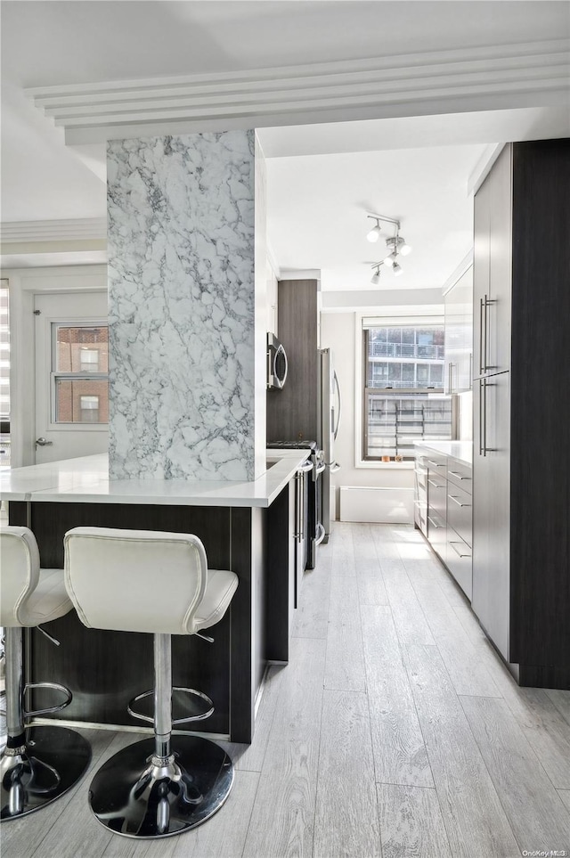 kitchen with a kitchen breakfast bar, kitchen peninsula, light hardwood / wood-style floors, and ornamental molding