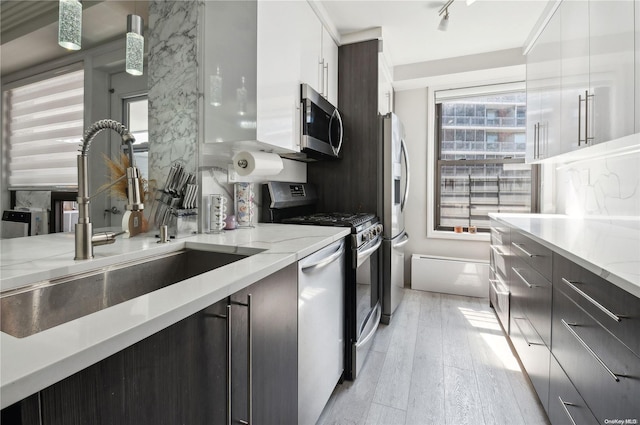 kitchen featuring light stone counters, stainless steel appliances, sink, decorative light fixtures, and light hardwood / wood-style floors