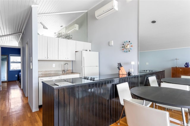 kitchen featuring light hardwood / wood-style floors, sink, an AC wall unit, white fridge, and white cabinetry