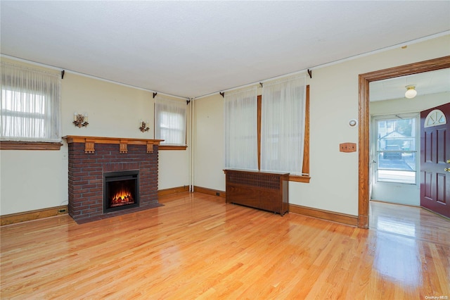 unfurnished living room with plenty of natural light, light hardwood / wood-style floors, and a brick fireplace