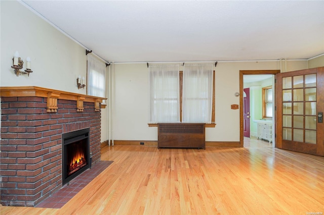 living room featuring light hardwood / wood-style floors, crown molding, radiator, and a brick fireplace