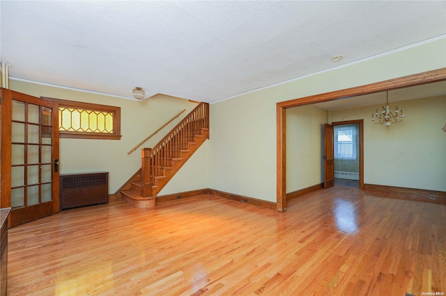 unfurnished living room featuring hardwood / wood-style floors, a chandelier, a textured ceiling, and a baseboard heating unit