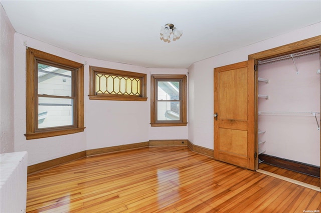 unfurnished bedroom featuring light hardwood / wood-style floors, radiator heating unit, a closet, and multiple windows