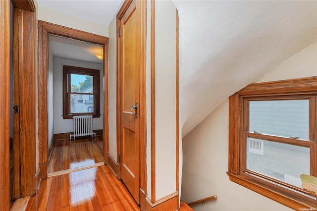 hallway with a textured ceiling, light hardwood / wood-style floors, vaulted ceiling, and radiator