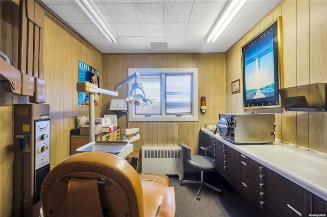 office area featuring wooden walls, radiator heating unit, and carpet