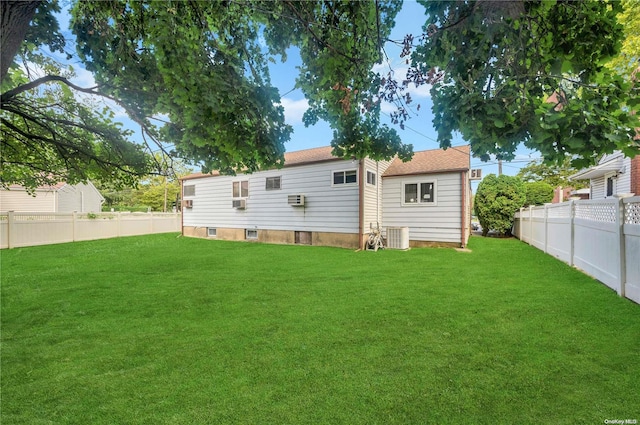 back of property featuring central air condition unit, a yard, and a wall mounted air conditioner