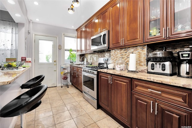 kitchen with sink, decorative backsplash, light tile patterned floors, light stone countertops, and appliances with stainless steel finishes