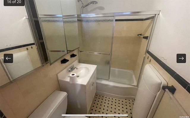 bathroom featuring vanity, bath / shower combo with glass door, and tile walls