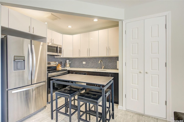 kitchen with white cabinetry, sink, backsplash, a breakfast bar area, and appliances with stainless steel finishes