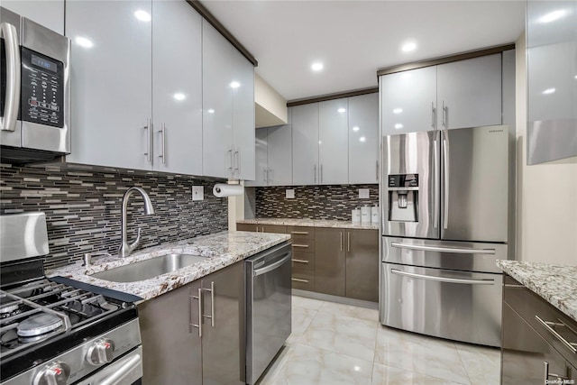 kitchen featuring decorative backsplash, appliances with stainless steel finishes, light stone counters, and sink