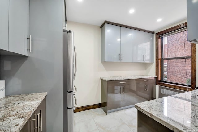 kitchen with gray cabinetry, stainless steel fridge, radiator heating unit, and light stone countertops