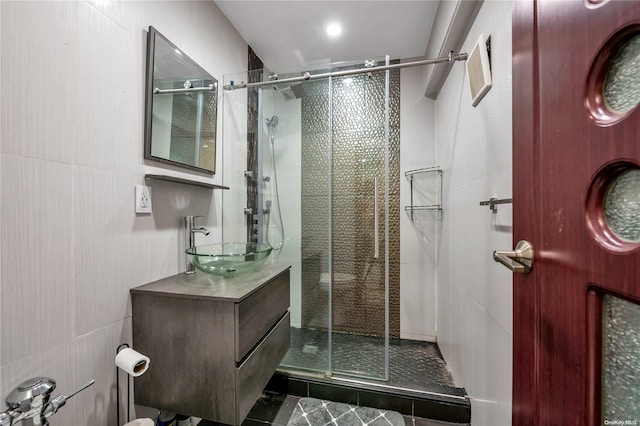 bathroom featuring tile patterned floors, vanity, a shower with shower door, and tile walls