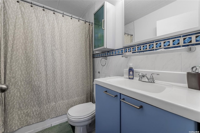 bathroom with a textured ceiling, vanity, toilet, and tile walls