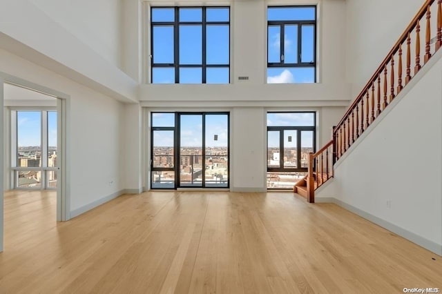 unfurnished living room with a high ceiling, light hardwood / wood-style flooring, and a wealth of natural light