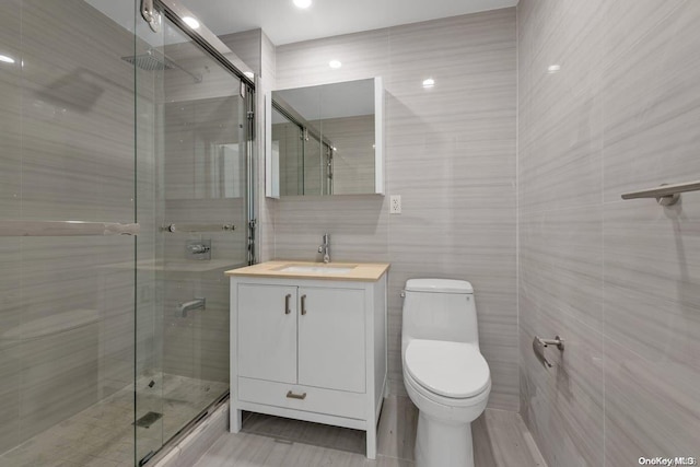 bathroom with walk in shower, vanity, tile walls, and toilet