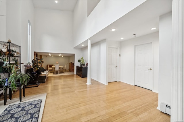 interior space featuring ornate columns, baseboard heating, a high ceiling, and light hardwood / wood-style flooring