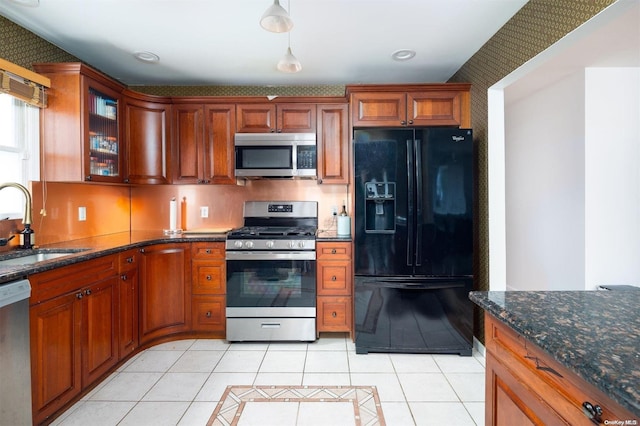 kitchen with decorative light fixtures, stainless steel appliances, dark stone countertops, sink, and light tile patterned floors