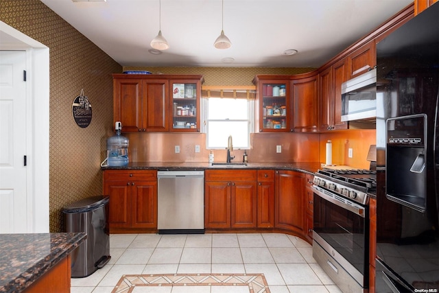 kitchen with stainless steel appliances, light tile patterned flooring, dark stone countertops, pendant lighting, and sink