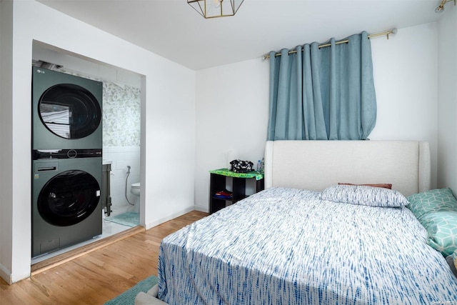 bedroom with wood-type flooring, ensuite bath, and stacked washer and dryer