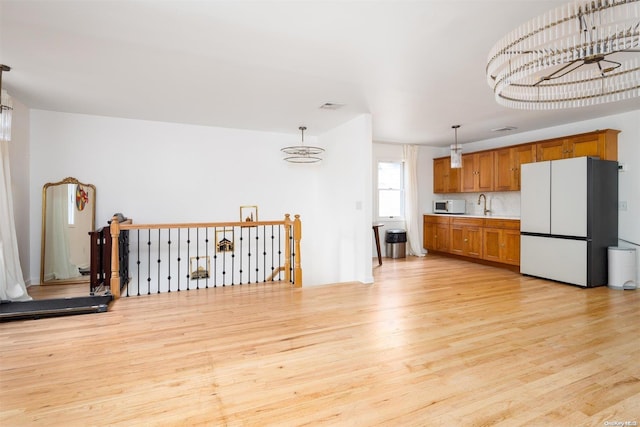 kitchen featuring pendant lighting, white appliances, tasteful backsplash, sink, and light hardwood / wood-style flooring