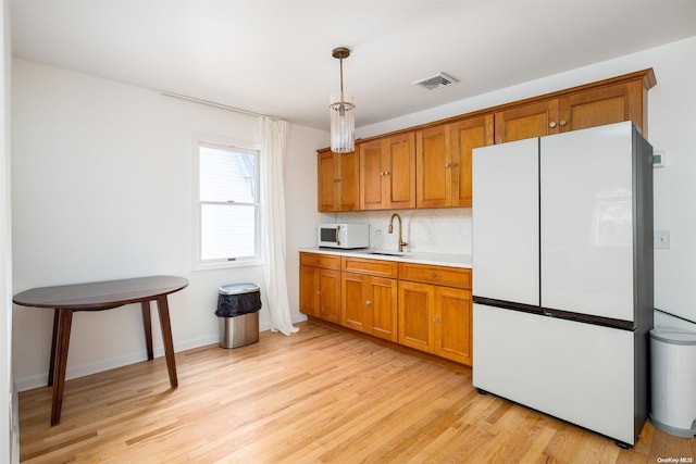 kitchen with tasteful backsplash, sink, white appliances, light hardwood / wood-style flooring, and hanging light fixtures