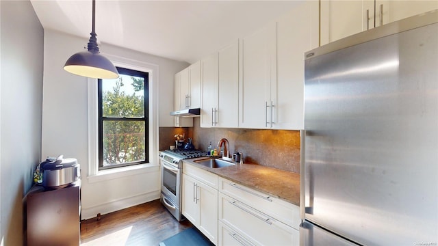 kitchen with appliances with stainless steel finishes, tasteful backsplash, dark wood-type flooring, sink, and decorative light fixtures