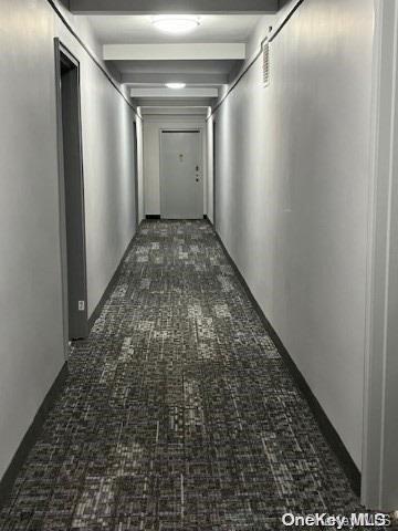 hall with beamed ceiling and dark colored carpet