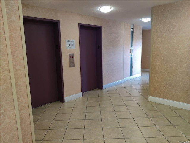 hall featuring light tile patterned flooring, a textured ceiling, and elevator