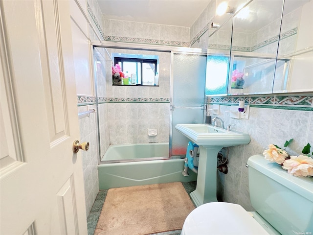 bathroom featuring combined bath / shower with glass door, toilet, and tile walls