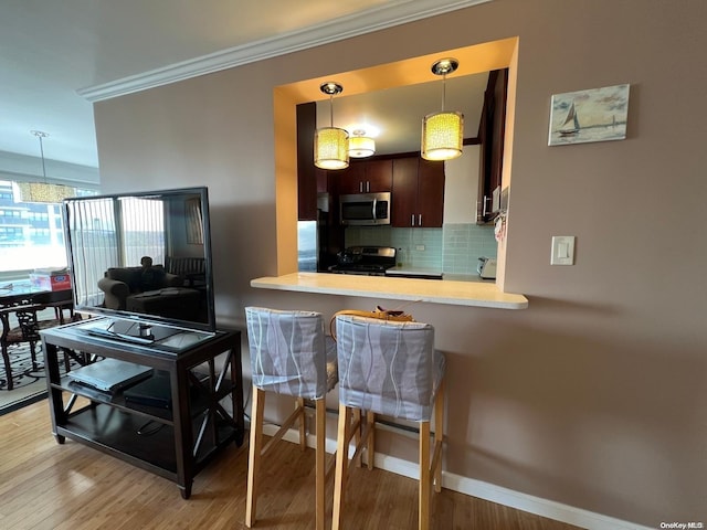 kitchen with dark brown cabinetry, stainless steel appliances, kitchen peninsula, decorative light fixtures, and light wood-type flooring