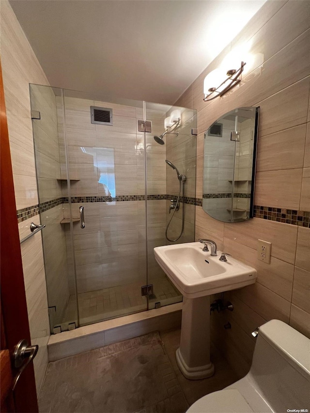 bathroom with a shower with door, tile walls, and toilet