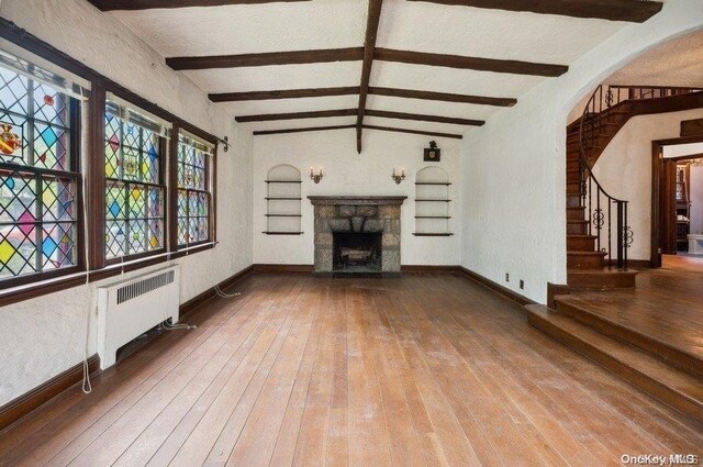unfurnished living room featuring radiator, lofted ceiling with beams, wood-type flooring, a textured ceiling, and a fireplace