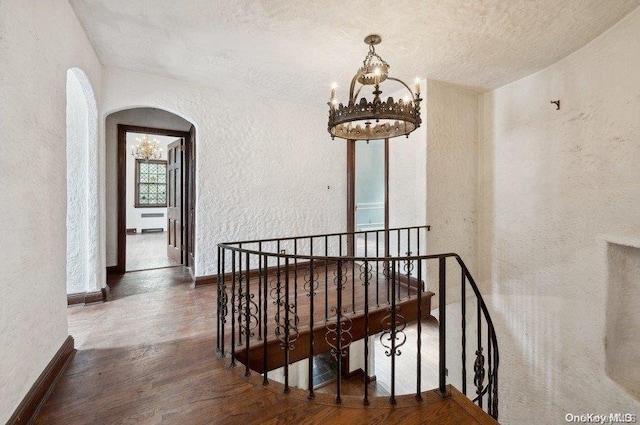 hallway featuring dark hardwood / wood-style flooring, a textured ceiling, and an inviting chandelier