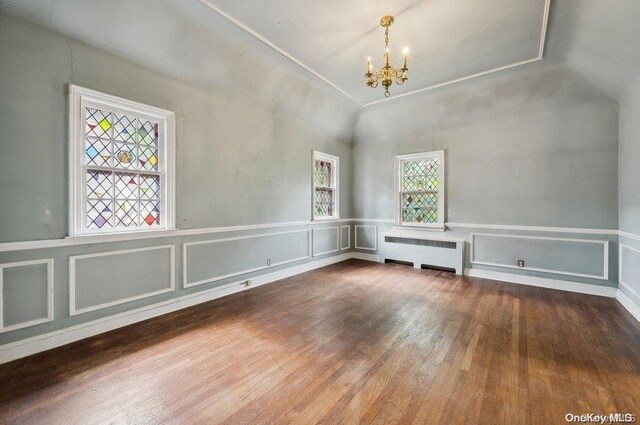 unfurnished room with a chandelier, radiator heating unit, hardwood / wood-style floors, and vaulted ceiling