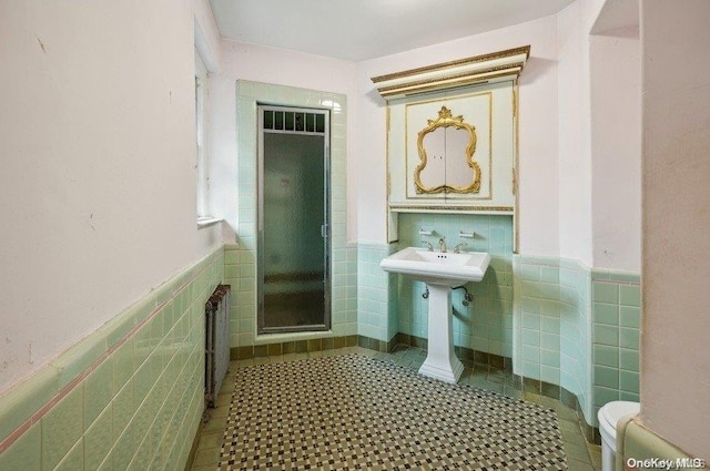 bathroom with radiator, tile patterned floors, sink, toilet, and tile walls