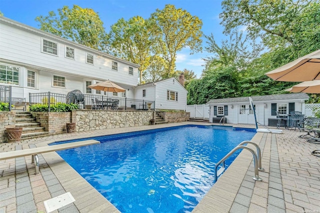 view of pool with a diving board, a patio area, and an outdoor structure