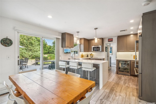 dining space with light wood-type flooring, sink, and beverage cooler