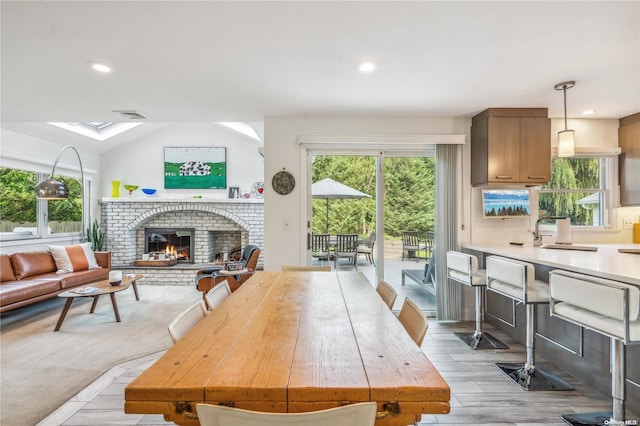 dining area with light hardwood / wood-style floors, sink, a fireplace, and vaulted ceiling