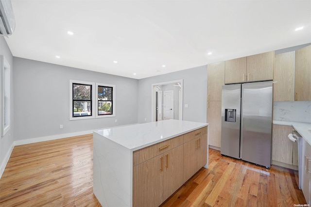 kitchen with light hardwood / wood-style flooring, stainless steel appliances, a wall unit AC, a kitchen island, and light brown cabinetry