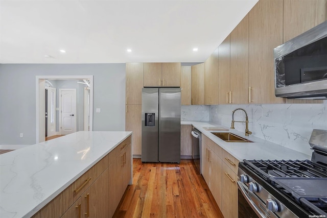 kitchen featuring sink, light wood-type flooring, appliances with stainless steel finishes, light stone countertops, and backsplash