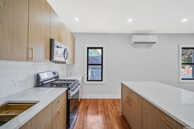 kitchen featuring backsplash, stainless steel appliances, a wall mounted AC, light hardwood / wood-style floors, and light stone countertops