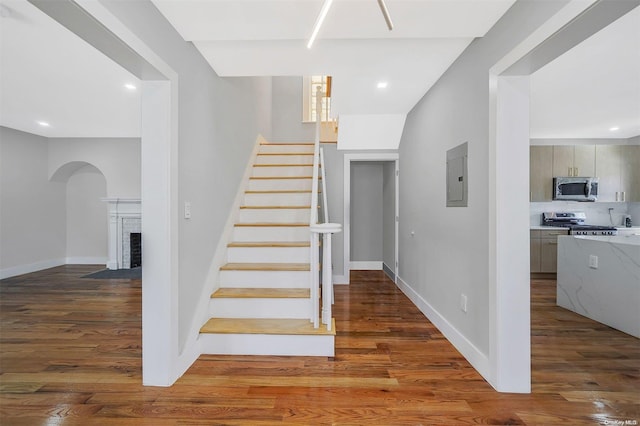 stairs with electric panel, hardwood / wood-style floors, and a brick fireplace