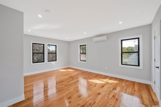 unfurnished room with a wealth of natural light, a wall mounted AC, and light wood-type flooring