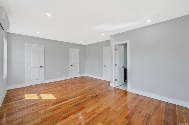 unfurnished bedroom featuring an AC wall unit and light hardwood / wood-style floors