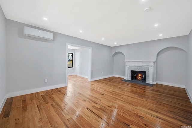 unfurnished living room featuring light hardwood / wood-style floors, a brick fireplace, and an AC wall unit