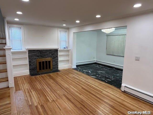 unfurnished living room with hardwood / wood-style floors, a baseboard radiator, and a stone fireplace