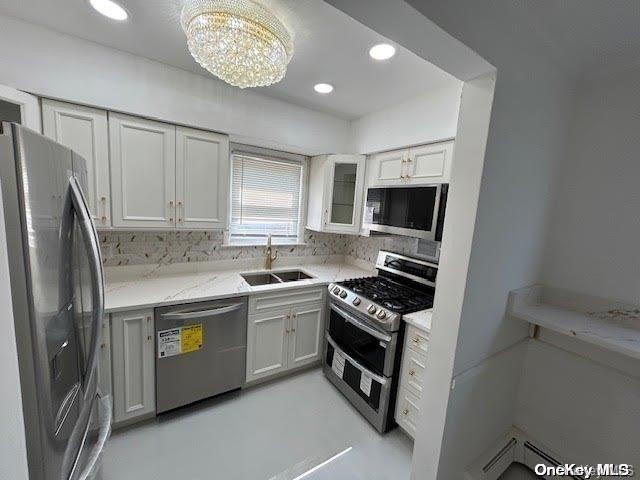 kitchen featuring a baseboard heating unit, an inviting chandelier, sink, decorative backsplash, and appliances with stainless steel finishes