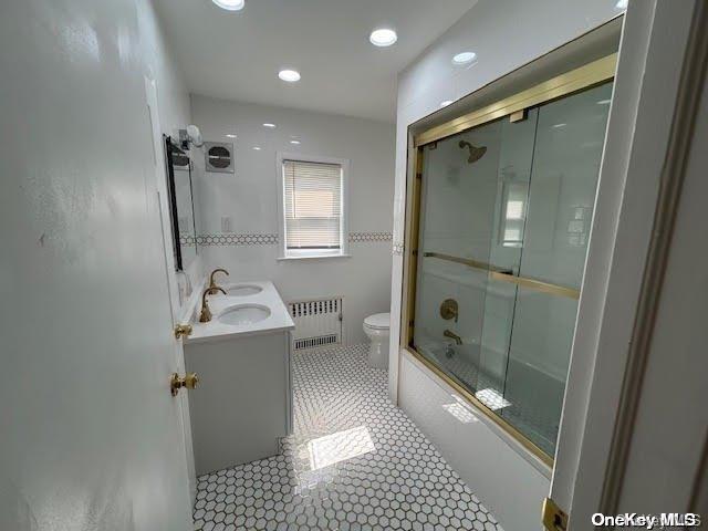 full bathroom featuring radiator, tile patterned flooring, bath / shower combo with glass door, toilet, and vanity